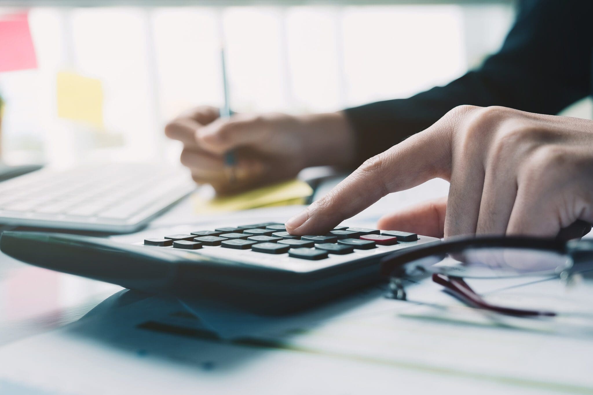 Businessman using a calculator and notepad to define key bid metrics for tendering
