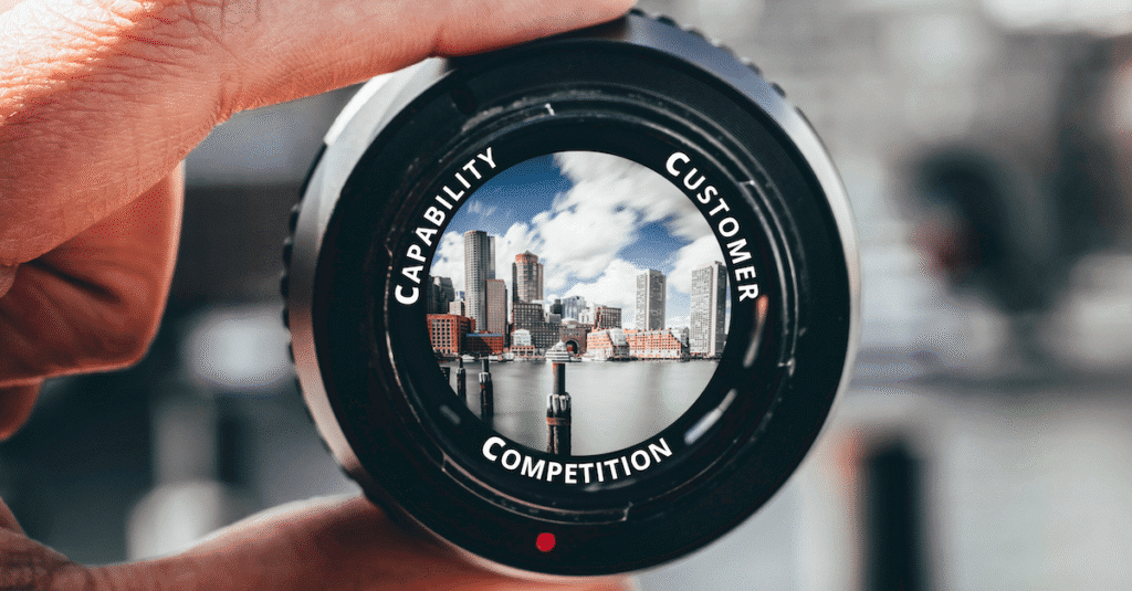 Looking through a camera lens with the Three Cs written around the edge - Customer, Competition and Capability